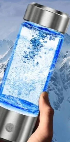 La botella AquaFusion en una mano, llena de agua con burbujas, tapa de acero inoxidable arriba y base de acero inoxidable con botón de encendido abajo, ante un fondo de montañas nevadas