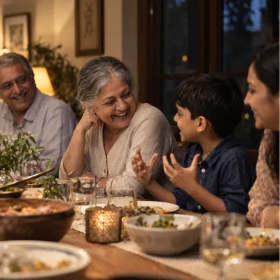 A woman in her early sixties laughing at a family dinner table, leaning in toward her eight-year-old grandson as he tells a story