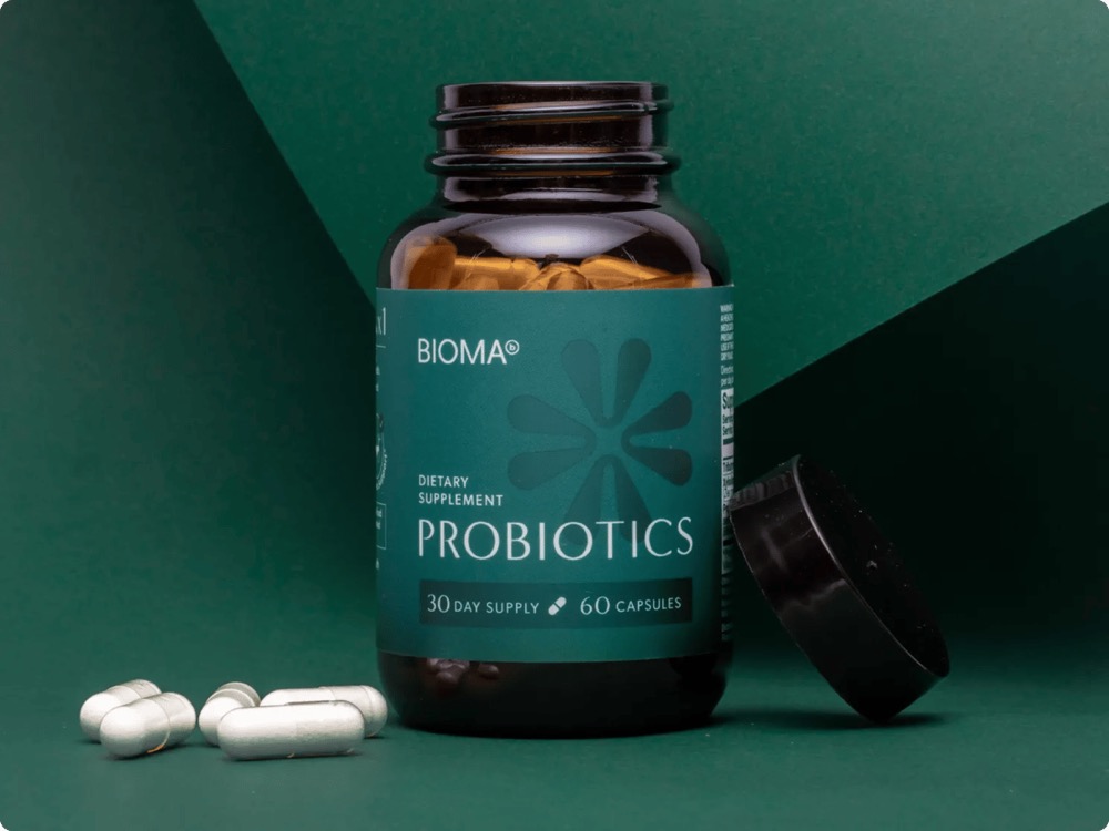 Bioma's own photo of the open bottle beside four white capsules on a green background
