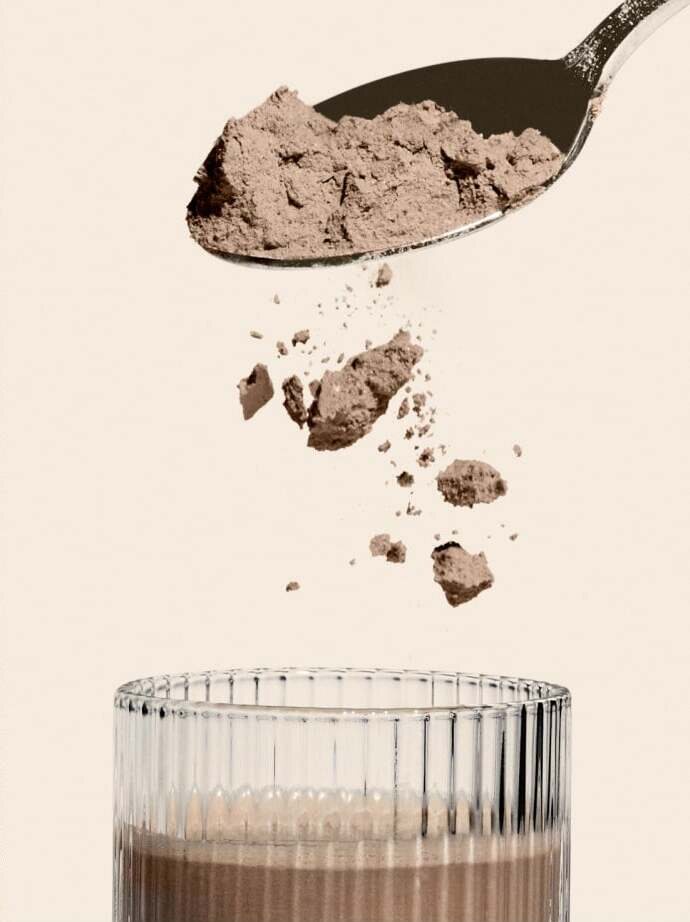 A spoonful of Free Soul powder falling into a ribbed glass already filled with the mixed shake