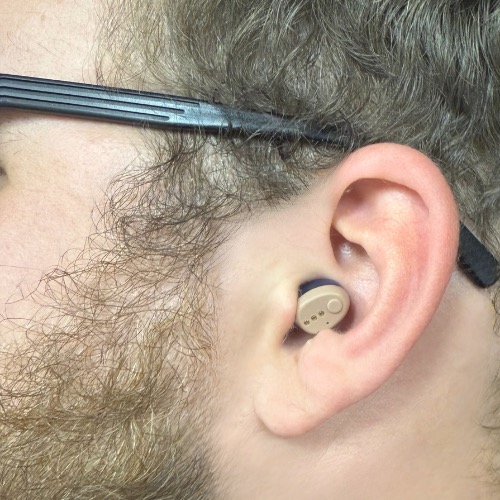 Hearing8s' own photo of one H2Go+ unit worn in an ear, with the arm of a pair of glasses resting above it