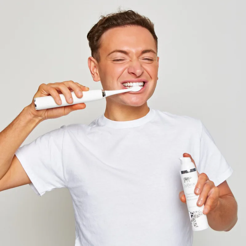 A man in a white T-shirt brushes with the Icy Bear sonic toothbrush while holding the Diamond Whitening Toothpaste, manufacturer's photo