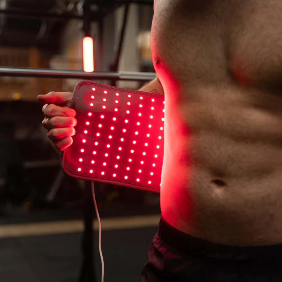 Close view of the lit Light Pad held against a bare torso in a gym, the individual red LED chips visible in even rows across the panel