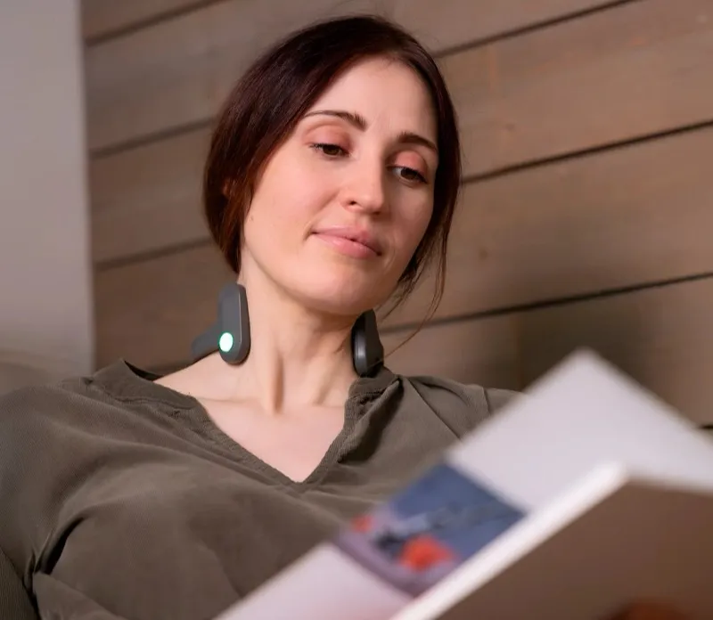 Frau liest abends ein Buch und trägt dabei das Pulsetto-Gerät im Nacken
