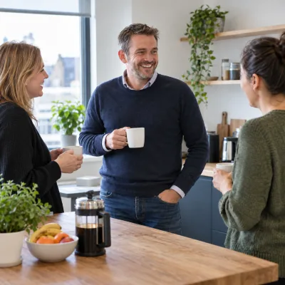 A man in his forties smiles while chatting with colleagues in a bright office kitchen